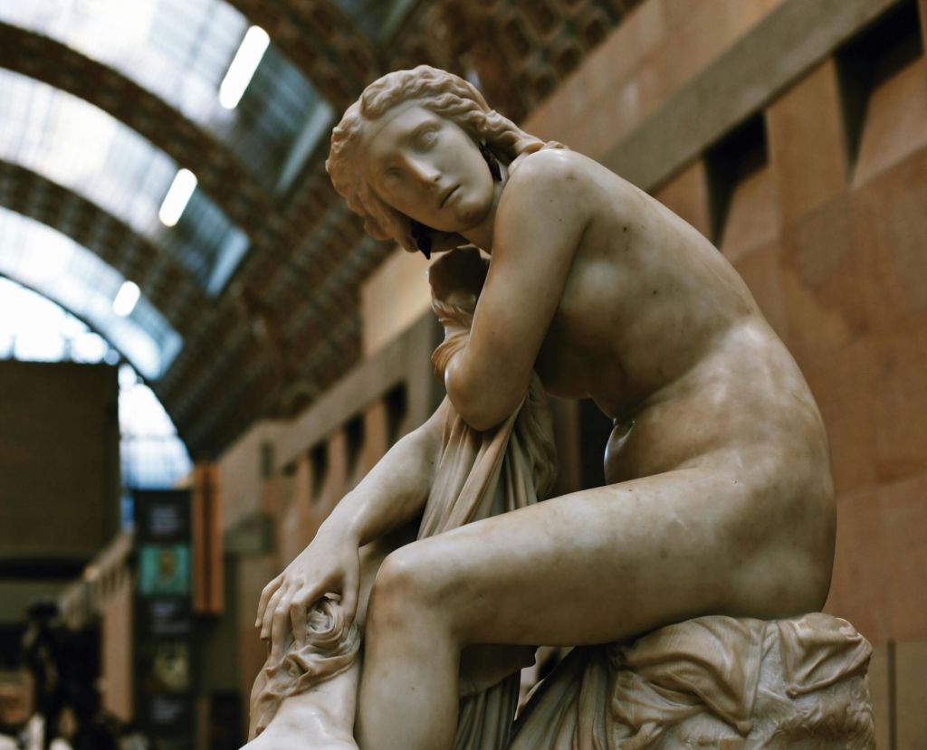 아치형 유리 패널 천장이 있는 박물관을 배경으로, 관상용 포즈로 장식된 좌석의 대리석 조각상.