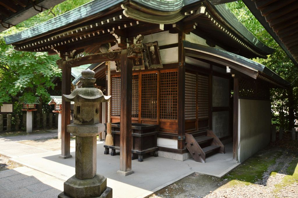 나무로 둘러싸인 전경에 석등이 있는 일본 전통 목조 신사입니다.