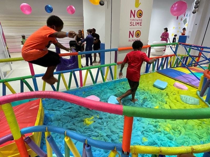 부드럽고 패딩 처리된 표면과 점액질 및 달리기를 금지하는 표지판이 있는 다채로운 실내 장애물 코스에서 놀고 있는 어린이.