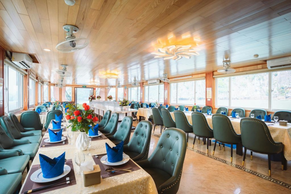 초록색 덮개를 씌운 의자, 파란색 냅킨이 세팅된 테이블, 따뜻한 조명 아래 꽃무늬 센터피스가 있는 넓고 우아한 식사 공간입니다.