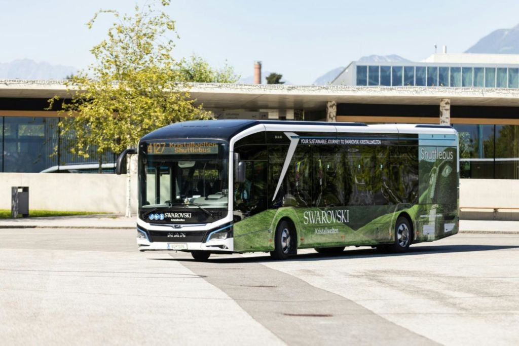 4127번 노선이 있는 스와로브스키 브랜드 셔틀 버스로, 맑은 하늘 아래 건물과 나무 근처의 버스 정류장에 주차되어 있습니다.