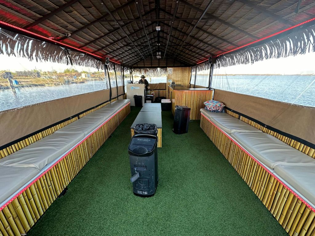 측면을 따라 자리한 야외 보트, 인조 잔디 바닥, 초가 지붕이 물가에 정박해 있습니다.