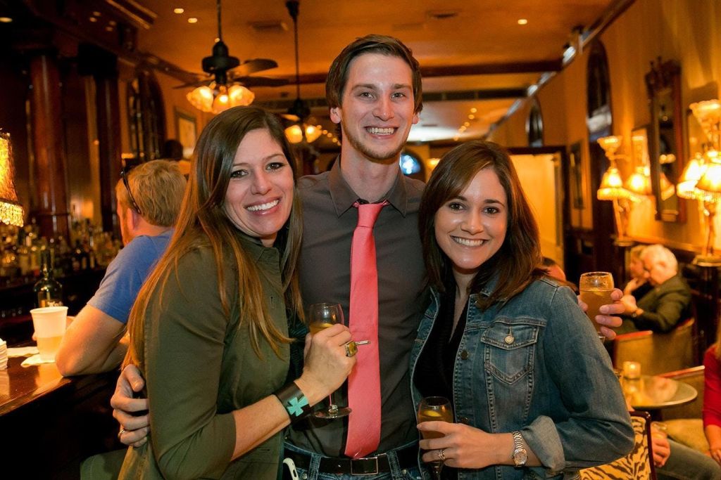 실내에서 함께 미소를 짓고 포즈를 취하는 세 사람이 따뜻한 분위기에서 음료를 들고 있습니다. 사교 모임일 가능성이 높습니다.