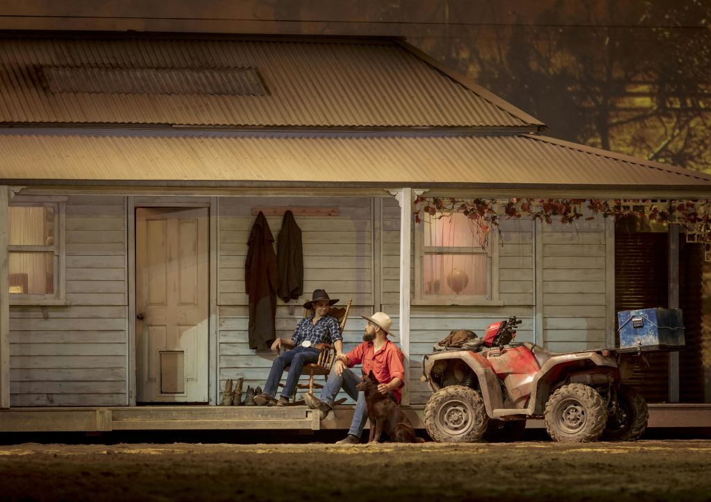 빨간색 ATV가 주차된 소박한 목조 주택 앞에 한 명은 앉아 있고 한 명은 개와 웅크리고 있습니다.