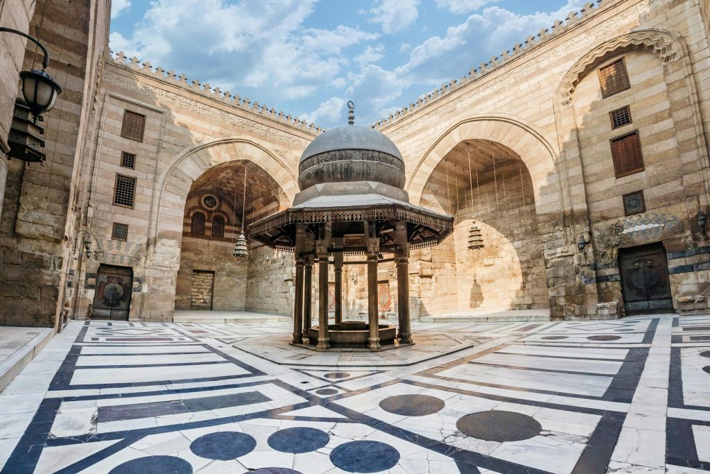 아치와 무늬 바닥이 있는 넓은 석조 안뜰에 돔형 지붕이 있는 화려한 야외 구조.