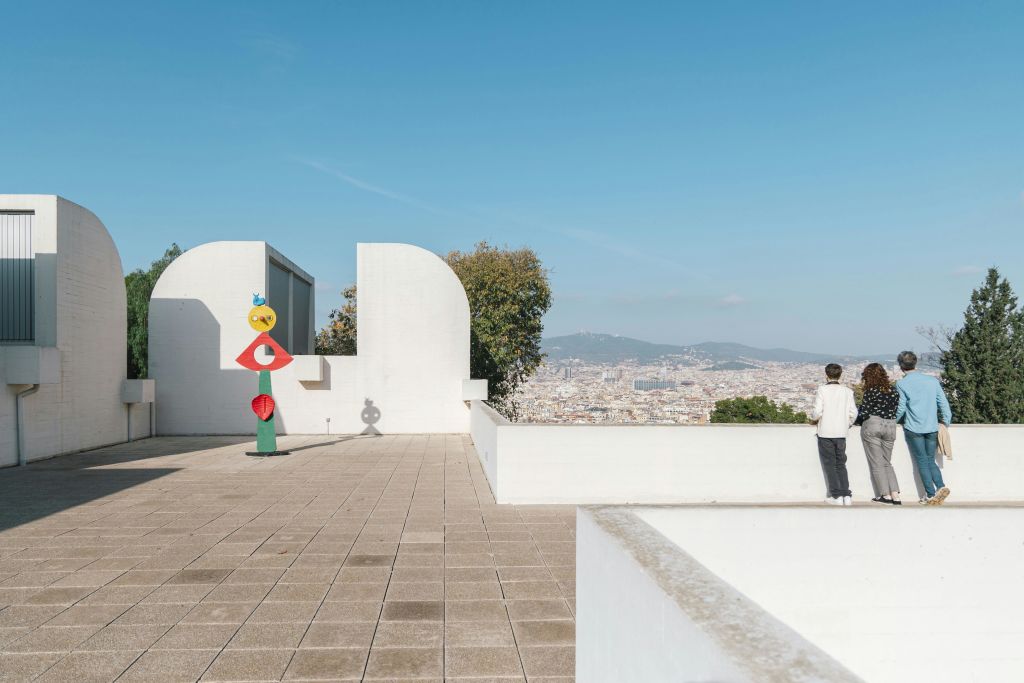 현대적인 조형물이 있는 옥상 테라스, 가장자리 근처에 서 있는 사람, 배경에 도시 풍경이 보입니다.