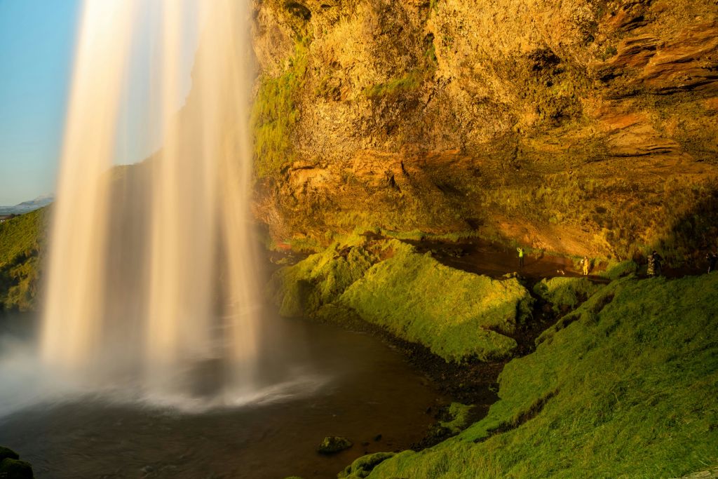 이끼로 뒤덮인 절벽 위로 폭포가 내리쬐고, 햇살이 그 광경을 비춥니다.