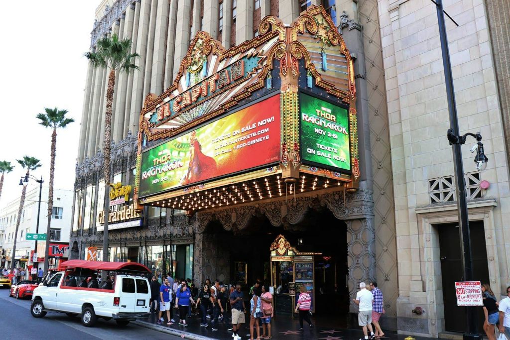 극장의 화려한 입구 앞에 서 있는 사람들은 영화 "토르: 라그나로크" 를 광고하는 마키를 들고 있습니다.