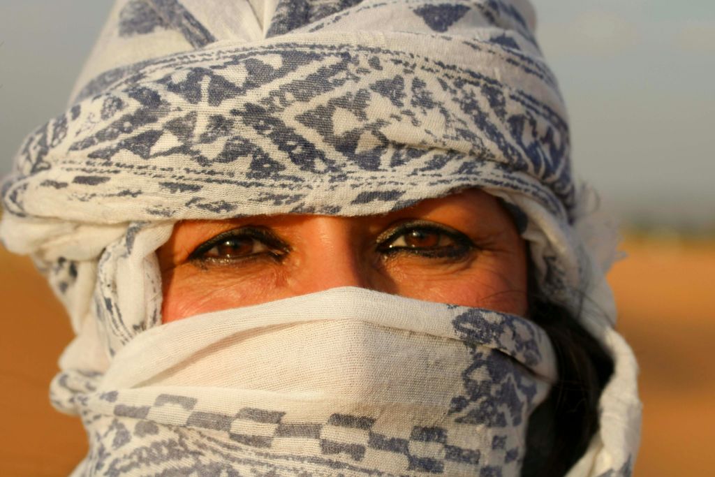 무늬가 있는 흰색과 파란색 천으로 부분적으로 가려진 진한 갈색 눈으로 사람의 얼굴을 클로즈업합니다.