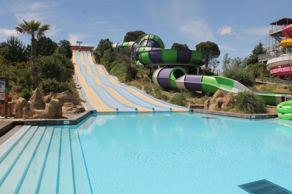 파란색과 노란색 직선 슬라이드, 녹색과 보라색 튜브 슬라이드를 포함한 여러 개의 워터 슬라이드가 있어 맑은 수영장으로 이어집니다.