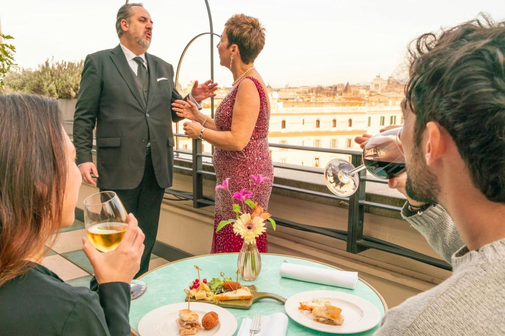 옥상에서 세 사람이 테이블 위에 음식과 음료를 놓고 대화를 나누고 있습니다. 두 사람은 관찰하는 동안 유리잔을 들고 대화를 나누고 있습니다.