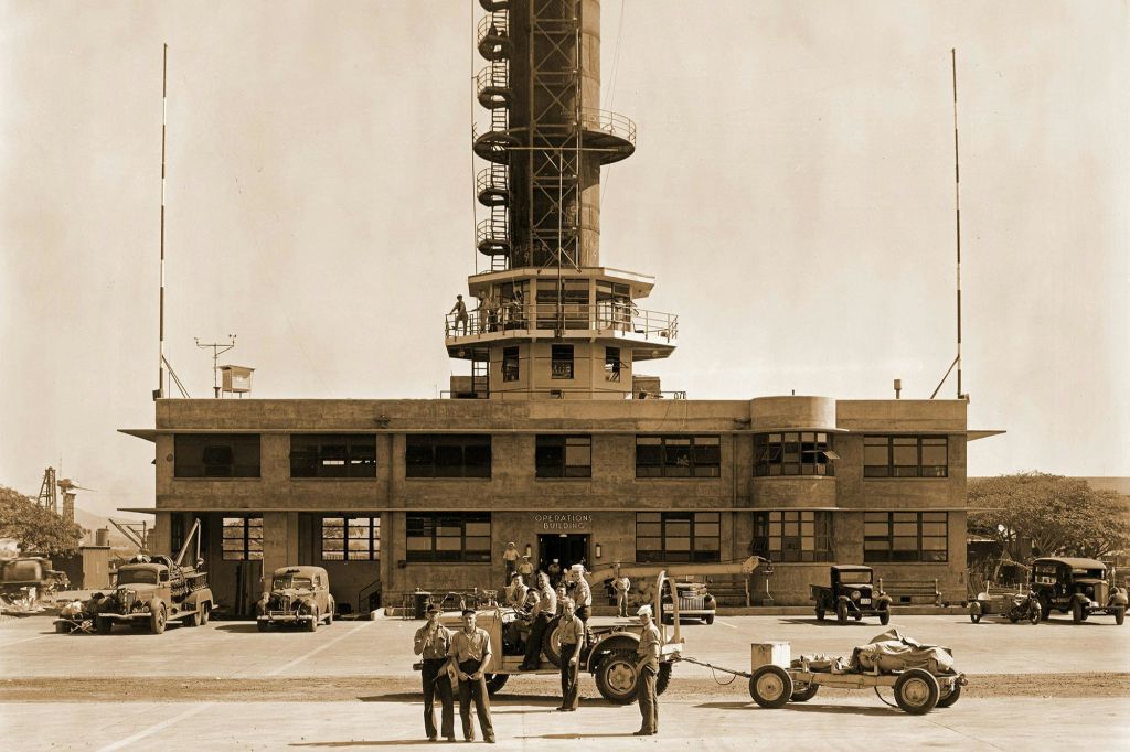 지프와 연료 트레일러를 포함한 여러 군인과 차량이 앞에 있는 컨트롤 타워의 세피아 톤 이미지.