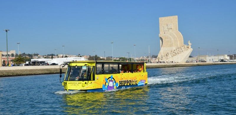 "HIPPOtrip" 이라는 이름의 노란색 수륙양용 투어 버스가 맑고 푸른 하늘 아래 커다란 석조 기념물 근처에 있습니다.