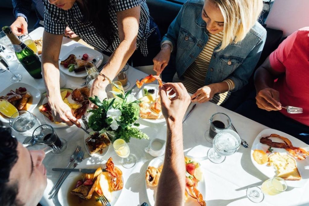 베이컨과 달걀, 커피와 물과 같은 음료를 포함한 음식 접시가 있는 테이블에서 아침 식사를 하는 세 사람.