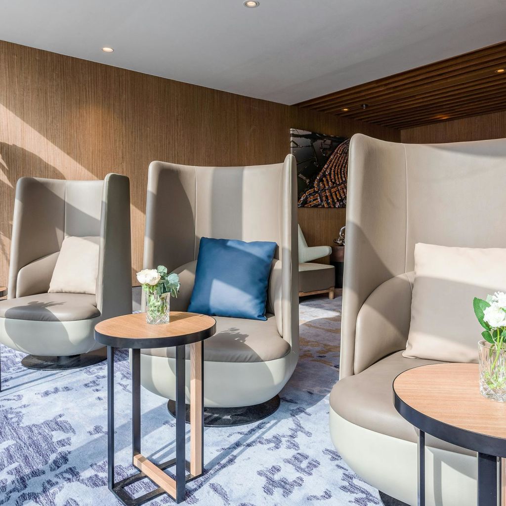 하이백 의자, 작은 원형 테이블, 꽃병이 있는 현대적인 라운지. 뉴트럴한 톤과 미니멀한 디자인.