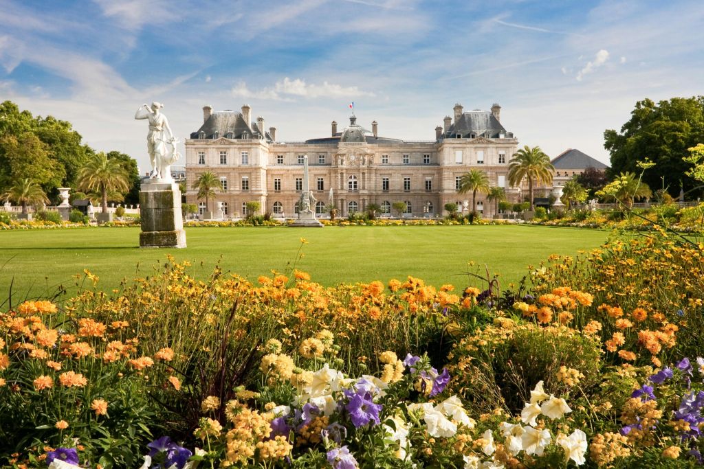 화려한 꽃이 만발한 정원, 잔디밭, 전경의 동상으로 둘러싸인 프랑스 국기가 있는 화려한 건물.