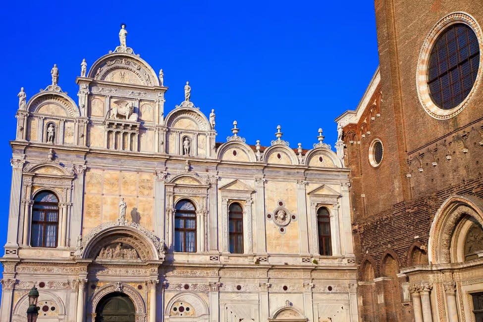밝고 푸른 하늘을 배경으로 화려한 건축물과 조각상이 있는 역사적인 건물입니다. 벽돌 구조가 오른쪽에 부분적으로 보입니다.