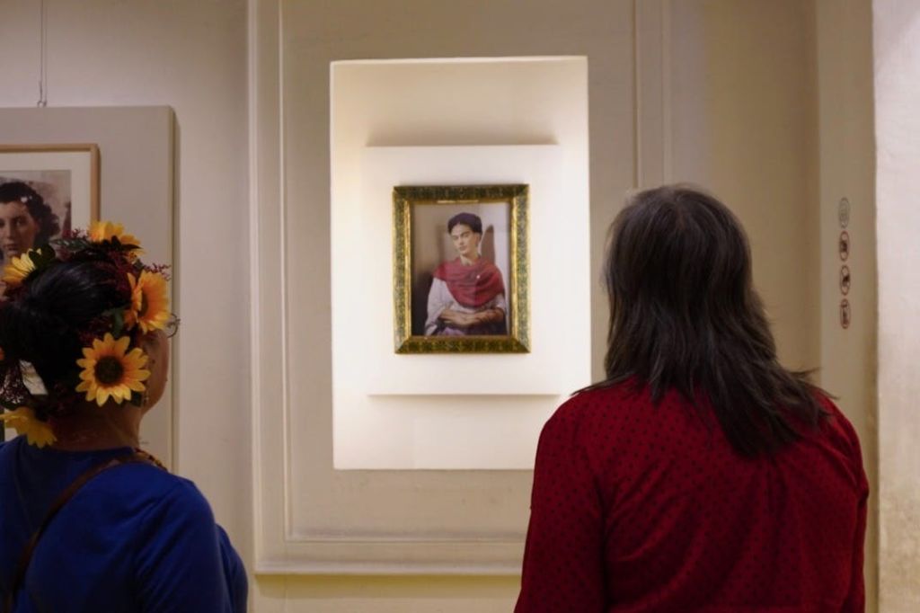 벽에 조명이 밝은 틈새시장에서 두 사람이 액자에 담긴 초상화를 바라보고 있습니다. 초상화 속 인물은 빨간색과 흰색을 입습니다.