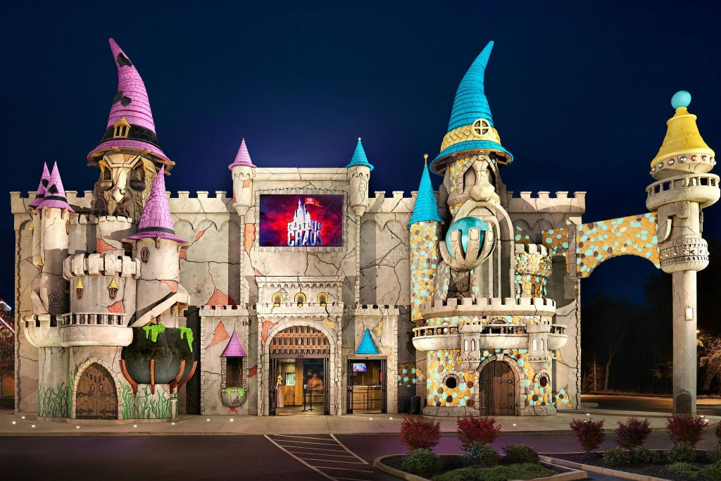 밝은 포탑과 두 개의 커다란 마법사 피규어가 있는 기발한 성 모양의 건물로, 하나는 파란색 모자가 있고 다른 하나는 분홍색 모자가 있습니다.