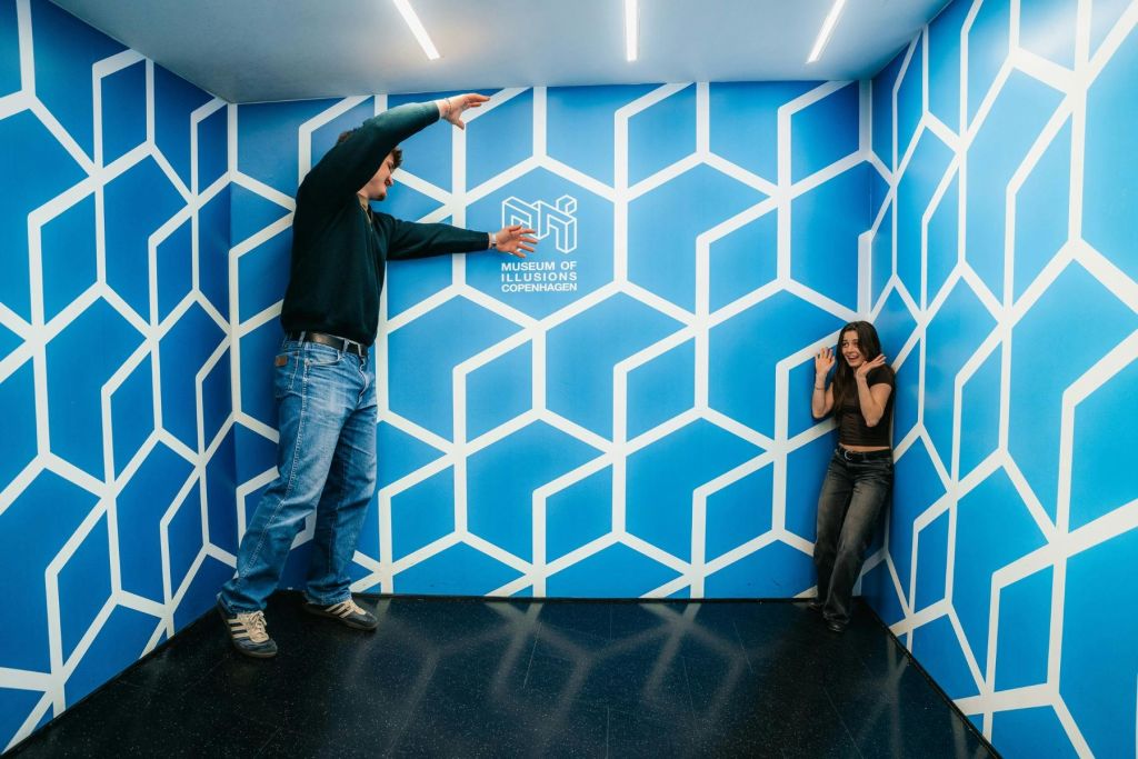 코펜하겐 환상 박물관의 기하학적 패턴이 있는 파란 방에서 장난스럽게 상호 작용하는 두 사람.
