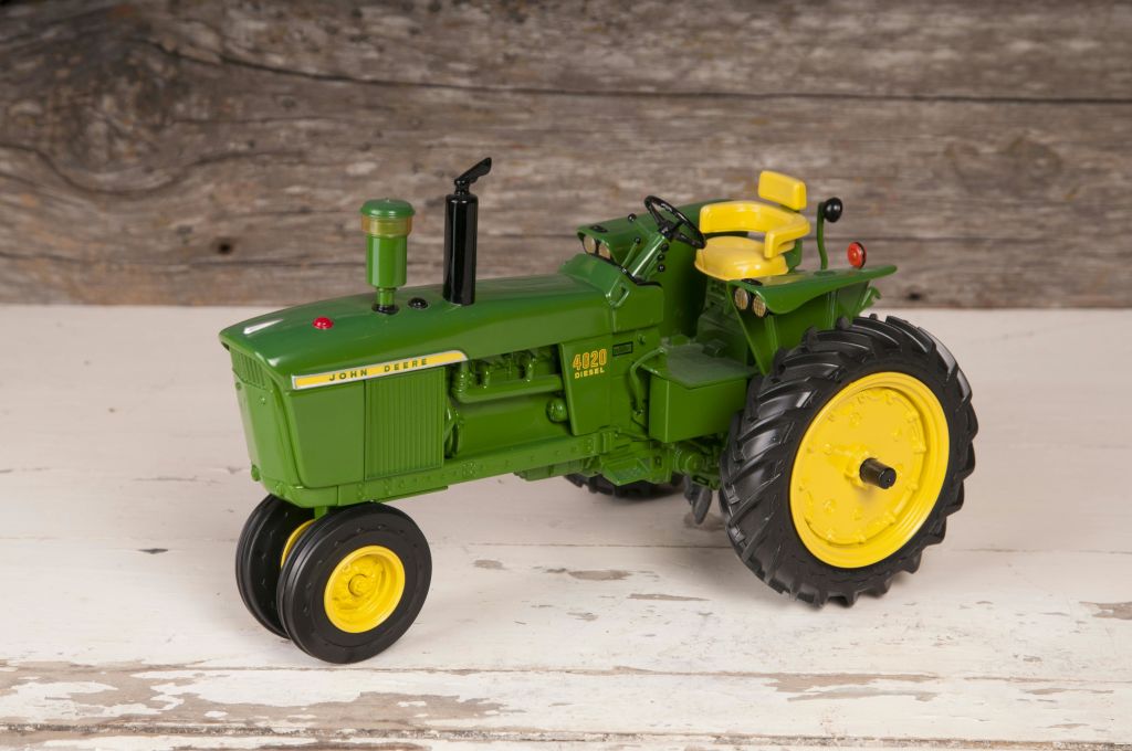목재 표면에 노란색 바퀴와 시트가 있는 녹색 John Deere 모델 4020 트랙터.