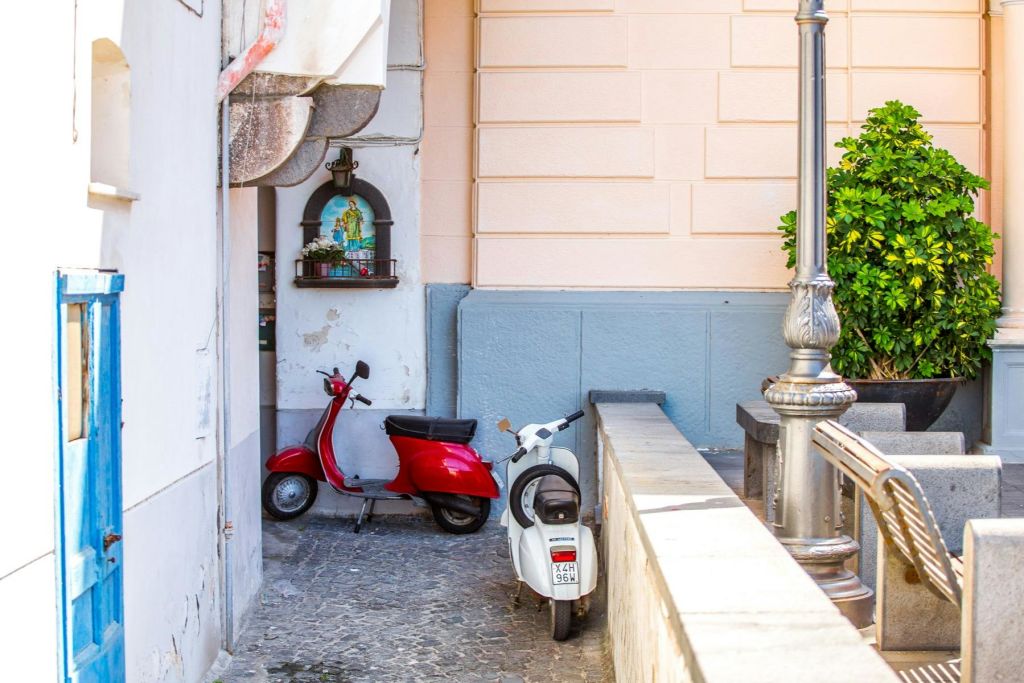 빨간색과 흰색 두 대의 스쿠터가 복숭아색 벽 옆 골목에 주차되어 있습니다.