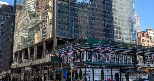 미국 국기를 전시하고 반사 유리 구조물로 둘러싸인 기지에 레스토랑이 있는 도시 건물입니다.