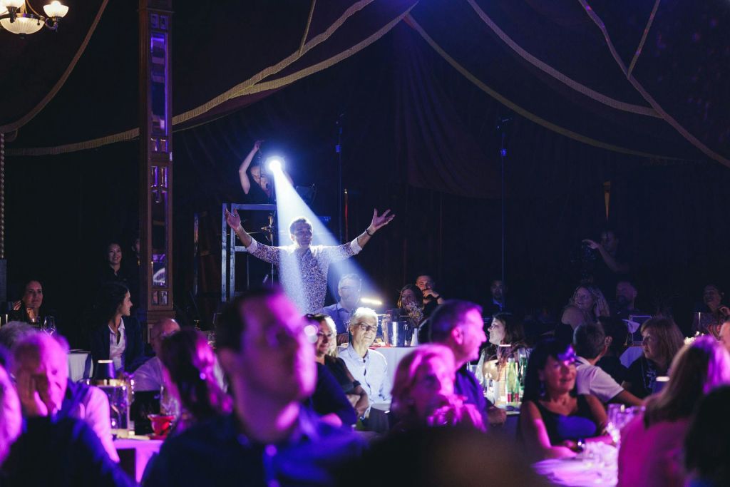 테이블과 좌석이 있는 붐비고 어두운 방에서 팔을 들고 있는 사람에게 스포트라이트가 비춰집니다.