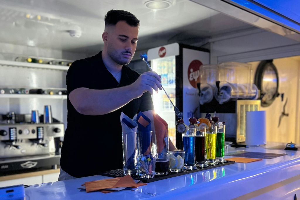 바에서 다채로운 음료와 유리잔으로 장식된 음료를 준비하는 바텐더가 바 장비로 둘러싸여 있습니다.