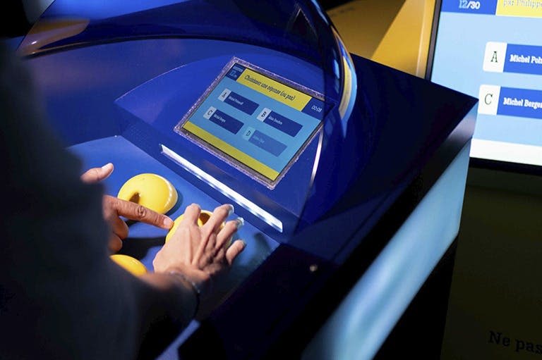 사람이 파란색 표면에서 터치스크린 디스플레이와 둥근 노란색 물체와 상호 작용하며, 이는 대화형 전시의 일부일 가능성이 높습니다.