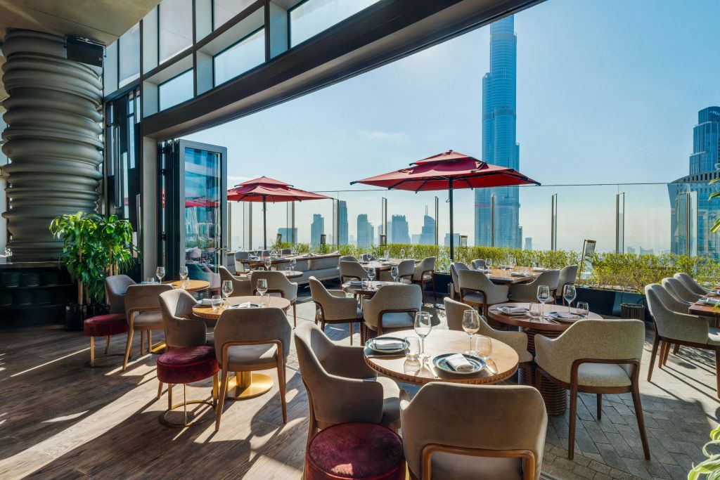 식사 테이블, 빨간 우산, 높은 고층 빌딩을 배경으로 한 도시의 스카이라인을 갖춘 현대적인 야외 레스토랑입니다.