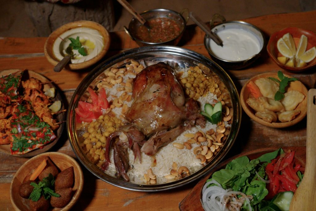 밥 위에 야채와 견과류를 곁들인 구운 고기 요리와 나무 상에 다양한 반찬과 소스를 곁들인 요리.