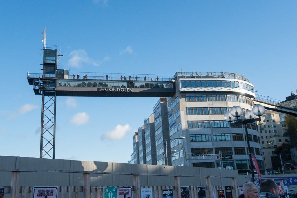 맑고 푸른 하늘 아래 '곤돌렌' 이라는 이름의 유리 통로가 있는 현대적인 건물로, 통로에 사람들이 보입니다.