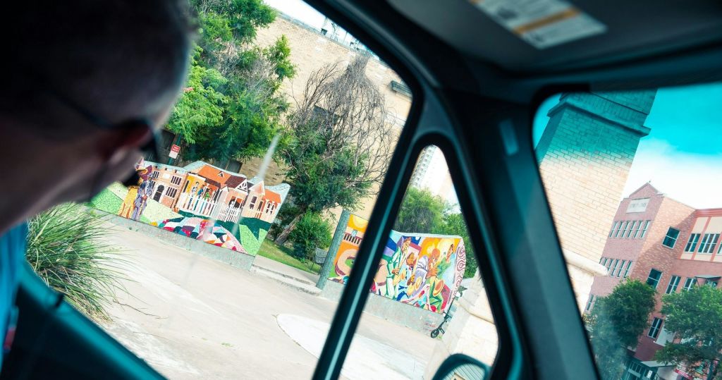 벽돌 건물을 배경으로 차량 창문 너머로 보이는 다채로운 벽화와 나무.