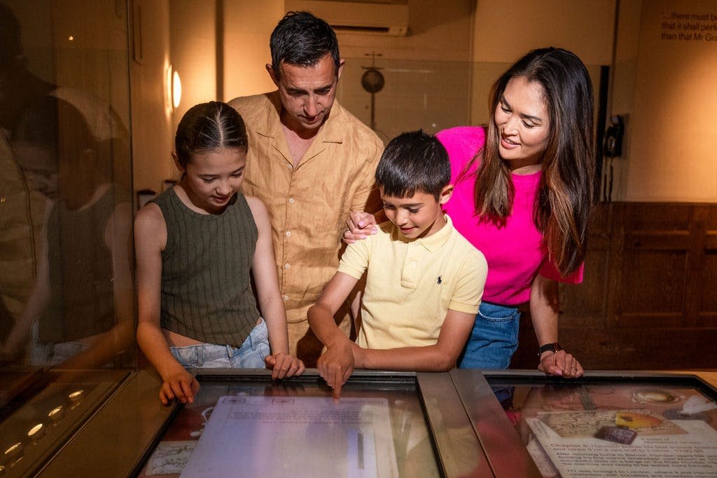 박물관이나 전시홀에서 전시 테이블을 바라보는 두 명의 성인과 두 명의 어린이.