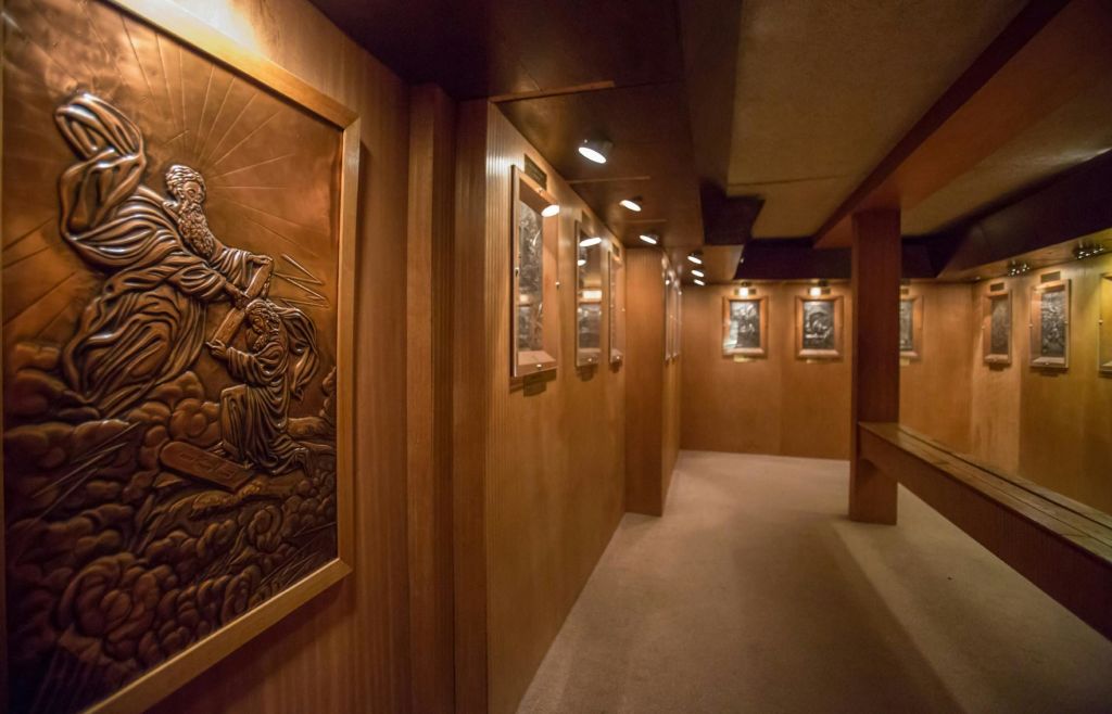 천장 스포트라이트 아래에서 액자에 담긴 장식용 청동 부조를 보여주는 나무 패널이 있는 희미한 조명 복도.