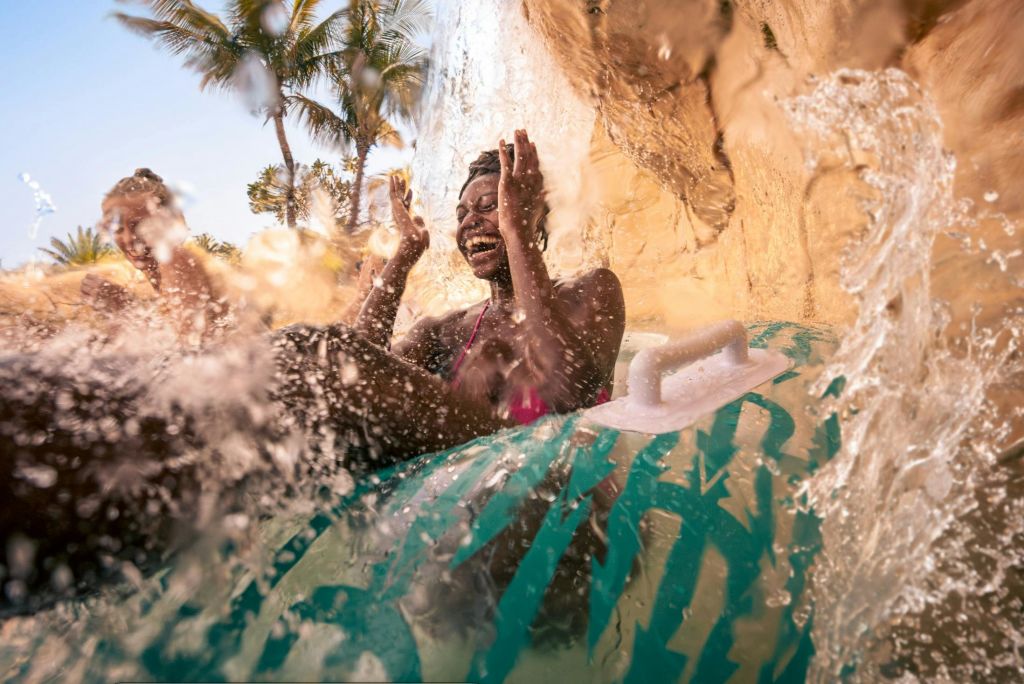 야자수를 배경으로 폭포 아래에서 워터 슬라이드를 즐기는 풍선 튜브를 탄 사람.