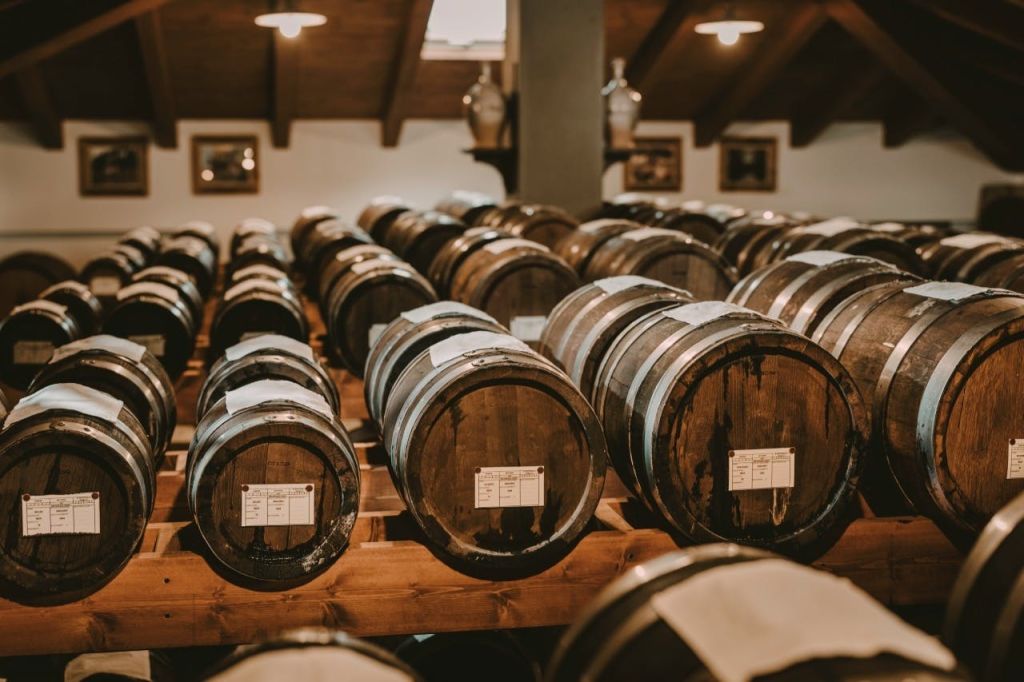 조명이 희미하고 소박한 지하실에 나무 대들보와 벽에 액자 그림이 있는 나무 통이 줄지어 있습니다.