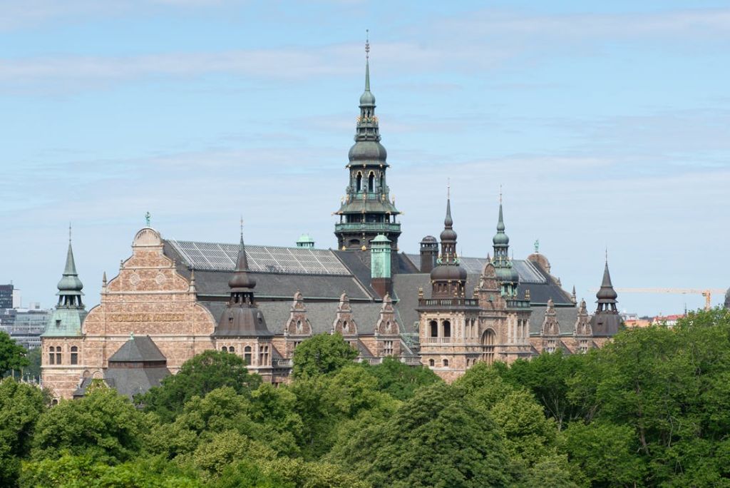 부분적으로 흐린 하늘 아래 푸른 나무로 둘러싸인 여러 개의 첨탑과 화려한 디테일이 있는 역사적인 건물.