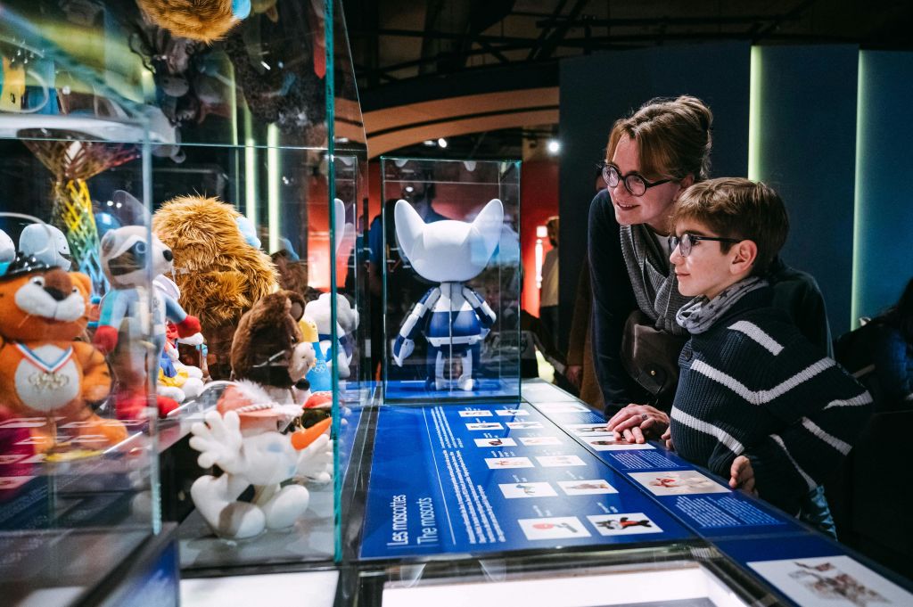 두 사람이 박물관 전시관에서 캐릭터 모델과 정보 패널이 있는 디스플레이 케이스를 바라보고 있습니다.