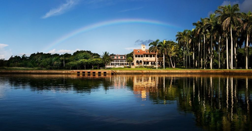 맑고 푸른 하늘을 배경으로 무지개가 일렬로 늘어선 집과 야자수가 우거진 고요한 호수.