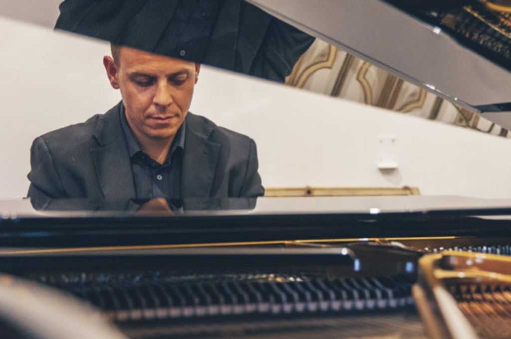 피아노의 열린 뚜껑을 통해 보이는 어두운 정장을 입은 남자는 실내에서 악기를 연주하는 데 집중했습니다.