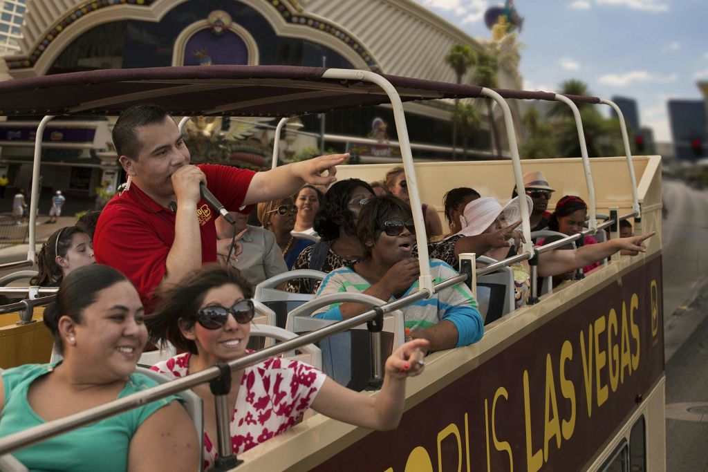 투어 가이드가 몸짓으로 마이크를 잡으며 이야기하고, 흥분한 승객 일행은 관광 버스 투어를 즐깁니다.