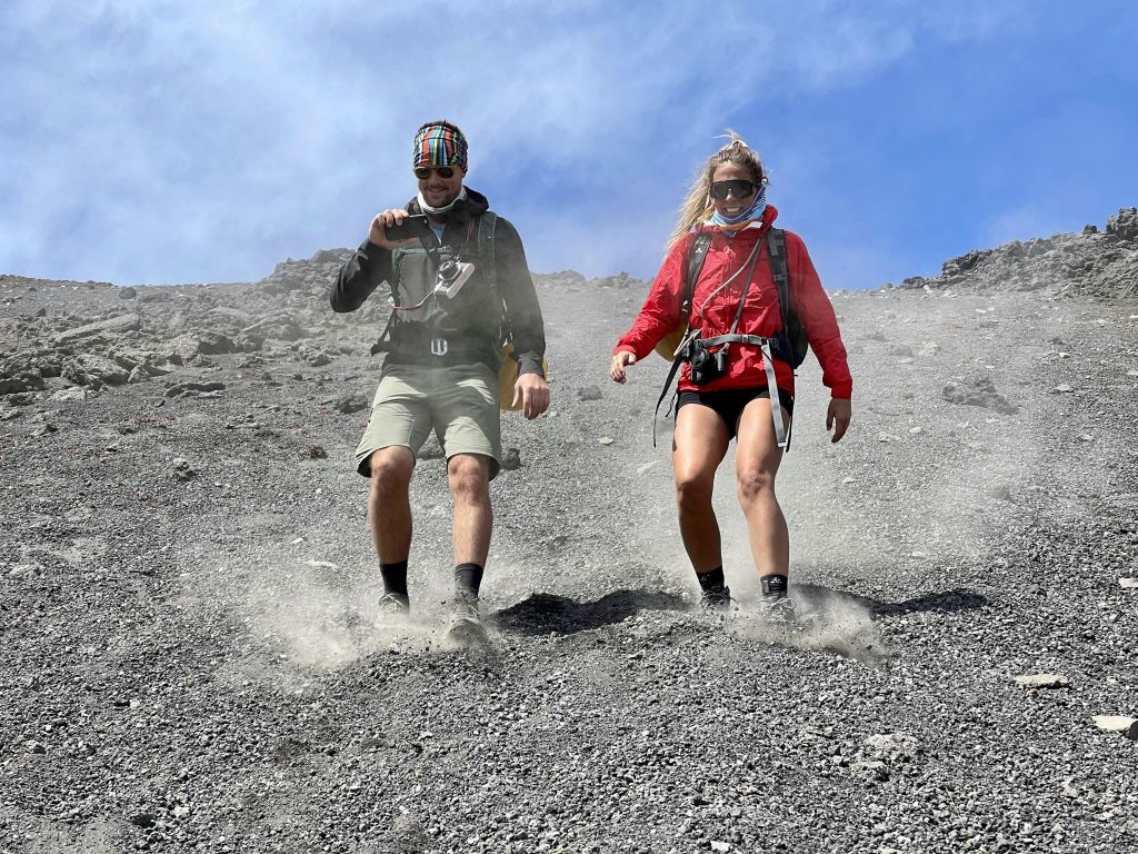 등산 장비를 착용한 두 사람이 맑고 푸른 하늘 아래 바위투성이의 먼지가 쌓인 경사면을 따라 내려오고 있습니다.