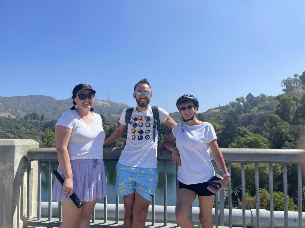 푸르름이 우거진 풍경과 맑고 푸른 하늘을 배경으로 다리에 서 있는 스포티한 복장의 세 사람.