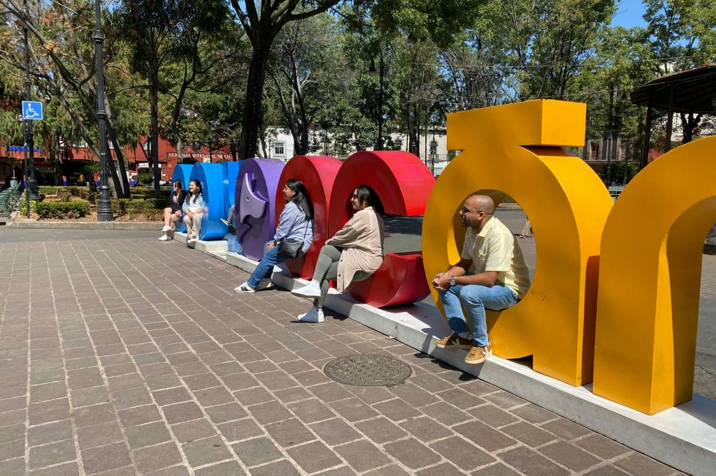 나무와 건물을 배경으로 공원에 배치된 크고 화려한 글자 조각 위에 다섯 사람이 앉아 있습니다.