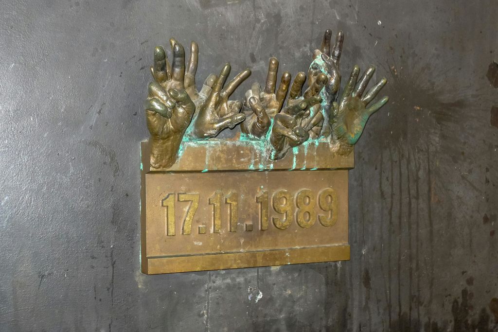 어두운 질감의 벽에 "17.11.1989" 날짜를 표시하는 명판 위에 손을 올린 청동 조각.