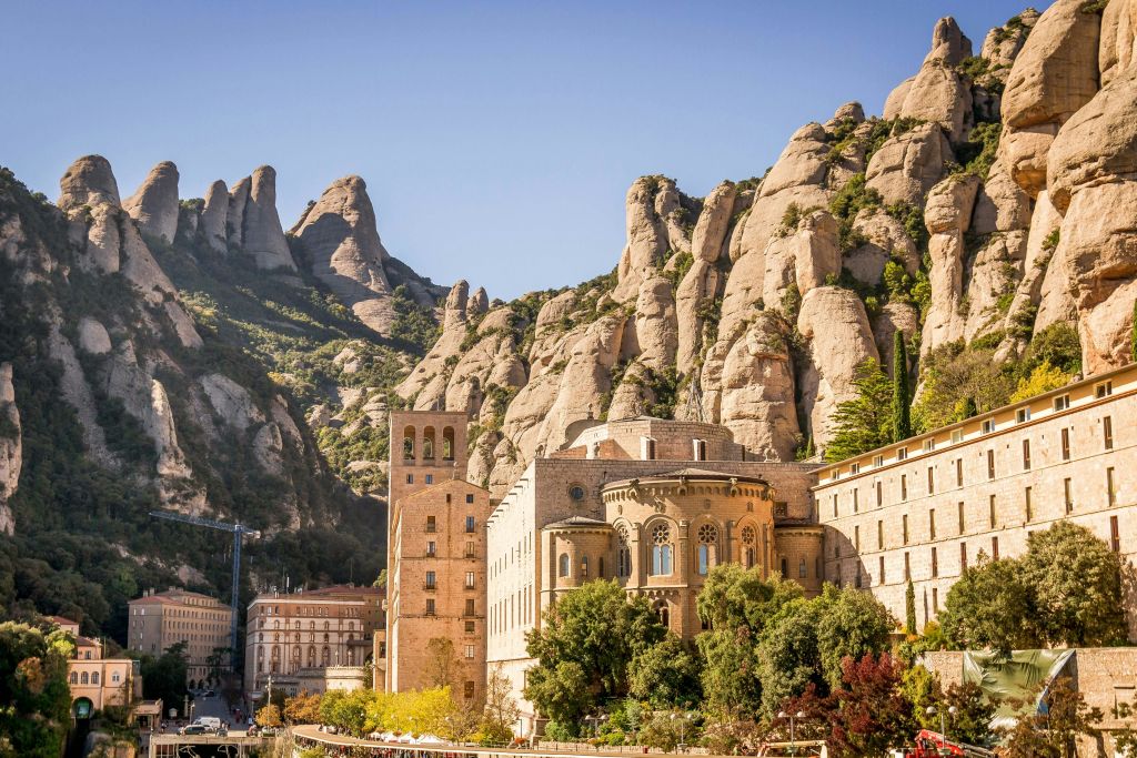 푸른 나무로 둘러싸인 탑이 있는 역사적인 석조 건물은 맑고 푸른 하늘 아래 험준한 산을 배경으로 합니다.
