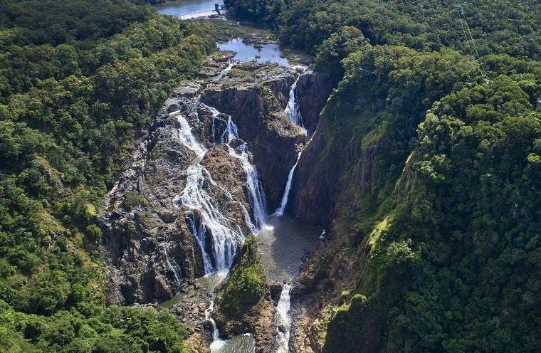 울창한 푸른 숲으로 둘러싸인 바위 절벽 아래로 이어지는 일련의 폭포의 공중 전망.