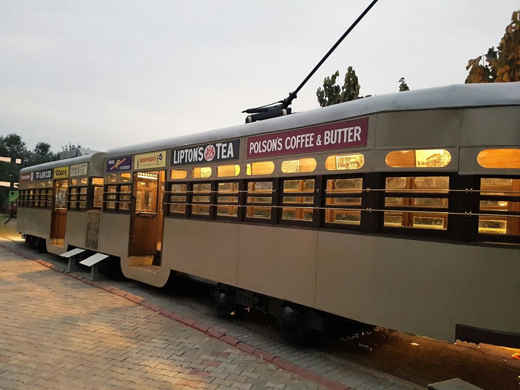포장된 산책로와 나무 옆에 주차된 "Lipton's Tea" 와 "Polson's Coffee & Butter" 광고가 있는 빈티지 트램입니다.